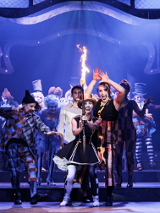 Zdjęcie ze spektaklu - grupa aktorów na scenie, na pierwszym planie aktorka trzymająca zapaloną pochodnię.