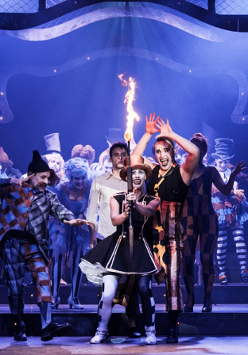 Zdjęcie ze spektaklu - grupa aktorów na scenie, na pierwszym planie aktorka trzymająca zapaloną pochodnię.