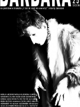 Czarno-białe zdjęcie z wysokim kontrastem. Osoba na zdjęciu ma założone futro, ma krótko obcięte kręcone włosy. Z rękawków wyłaniają się kościste dłonie z długimi, zaniedbanymi paznokciami