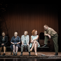 Zdjęcie z przedstawienia - cztery kobiety siedzące na ławce, na skraju ławki mężczyzna, który stoi i jedną nogą opiera się o ławkę.