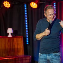 Mężczyzna występuje na scenie, trzyma mikrofon w ręku.