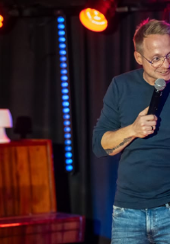 Mężczyzna występuje na scenie, trzyma mikrofon w ręku.