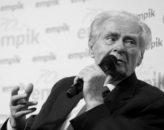 Starszy mężczyzna mówi do mikrofonu na spotkaniu z czytelnikami.