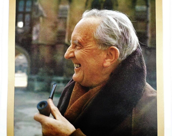 Starszy mężczyzna pali fajkę. Uśmiecha się. Ma zmarszczki koło oczu i łysinę.