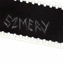 Grafika przypomina otwarty zamek błyskawiczny. W otwartej przestrzeni widać czarne tło z wydrapanym napisem "szmery".