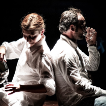 Kobieta i mężczyzna, siedzą obróceni do siebie plecami. Kobieta nalewa z czajnika wodę do szklanki, mężczyzna pije wodę ze szklanki.