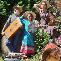 Mężczyzna i kobiety w średnim wieku ubrani w kolorowe stroje. Na głowach mają słomkowe kapelusze a w rękach trzymają różne instrumenty muzyczne. Przed nimi leżą inne instrmenty. Za nimi drzewa i kolorowe kwiaty.