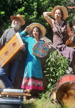 Mężczyzna i kobiety w średnim wieku ubrani w kolorowe stroje. Na głowach mają słomkowe kapelusze a w rękach trzymają różne instrumenty muzyczne. Przed nimi leżą inne instrmenty. Za nimi drzewa i kolorowe kwiaty.