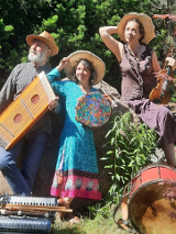 Mężczyzna i kobiety w średnim wieku ubrani w kolorowe stroje. Na głowach mają słomkowe kapelusze a w rękach trzymają różne instrumenty muzyczne. Przed nimi leżą inne instrmenty. Za nimi drzewa i kolorowe kwiaty.