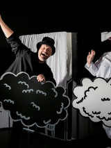 Zdjęcie, na czarnym tle, stoją aktorzy w czarno - białych strojach i trzymają w rękach czarne i białe chmurki.