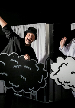 Zdjęcie, na czarnym tle, stoją aktorzy w czarno - białych strojach i trzymają w rękach czarne i białe chmurki.