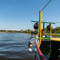 Dziób statku na Warcie. Widoczna kotwica. W dali widać most.