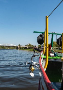 Dziób statku na Warcie. Widoczna kotwica. W dali widać most.