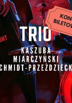 Zdjęcie przedstawia plakat koncertu jazzowego. Przedstawia trio muzyków występujących na scenie. Muzycy grają na kontrabasie, perkusji i fortepianie. Plakat jest czerwono-czarny i zawiera duży bilet z napisem "KONCERT BILETOWAN". Plakat zawiera również nazwiska muzyków: Kaszuba, Miarczyński i Schmidt-Przeździecka. Całość oddaje dynamiczną i żywą atmosferę występu jazzowego na żywo.