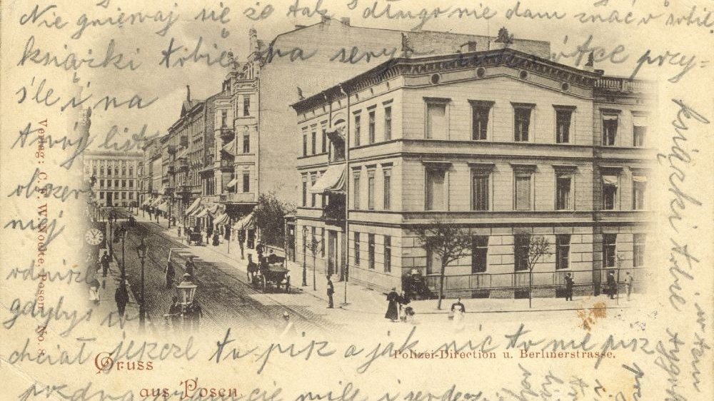 Pożółkła stara pocztówka ze zdjęciem miasta w centrum, zapisana odręcznym pismem.