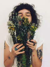 Młoda kobieta trzyma w ręku bukiet roślin i wdycha ich zapach.