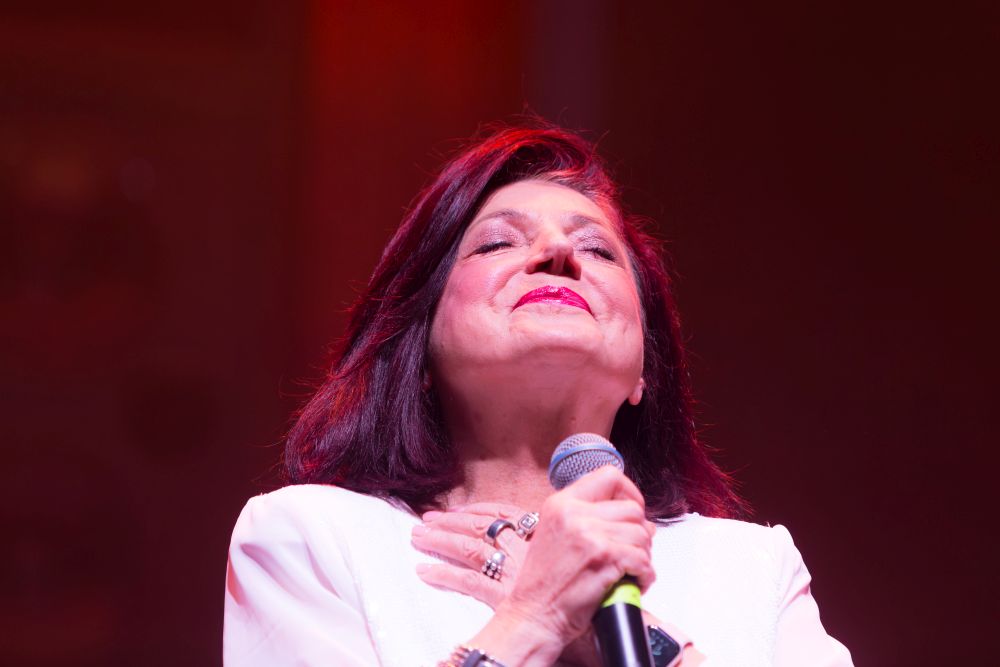 Urszula Dudziak z zamkniętymi oczami, skrzyżowanymi na piersi dłoniami, uśmiecha się.