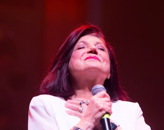 Urszula Dudziak z zamkniętymi oczami, skrzyżowanymi na piersi dłoniami, uśmiecha się.