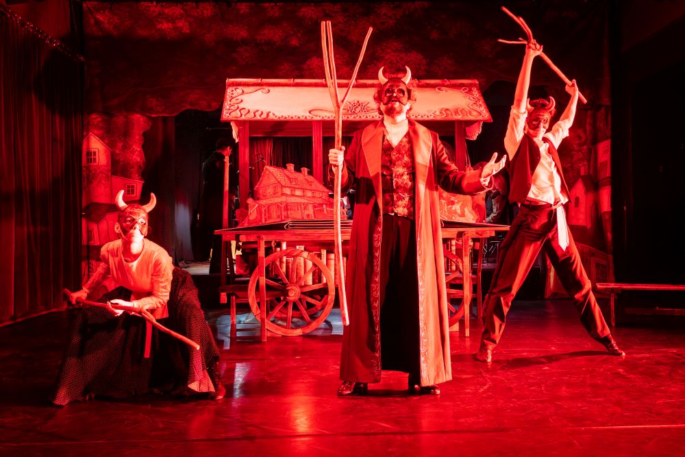 Uśmiechnięty mężczyzna w złotej kamizelce i białej koszuli siedzi na scenie.