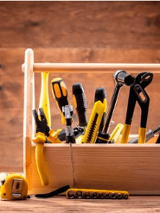 Zdjęcie drewnianej skrzyneczki wypełnionej różnymi narzędziami: młotkiem, śrubokrętami, kluczami...