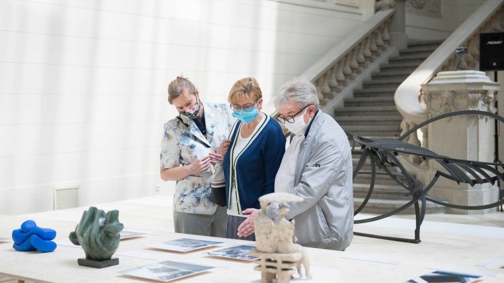 Na zdjęciu znajdują się trzy kobiety oglądające wystawione na białym stole eksponaty. W tle widać schody Muzeum Narodowego.