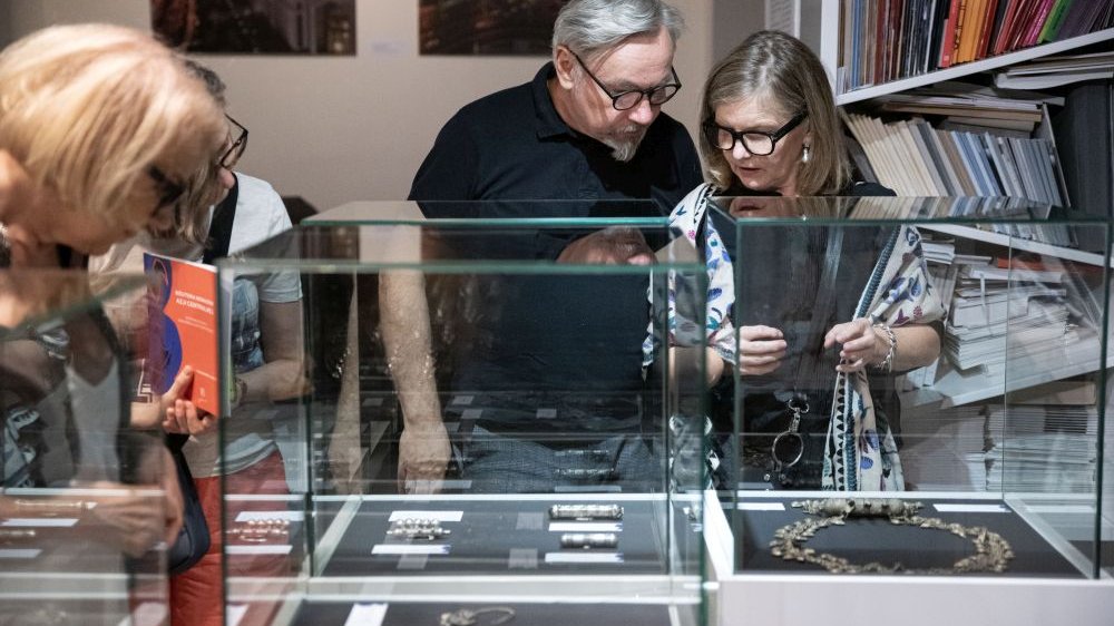 Zwiedzający wystawę oglądają biżuterię przez szklane gabloty.