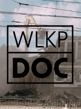 Napis o treści wlkp doc, w tle zdjęcie wyburzanej kamienicy z widoczną rozwartą łyżką koparki i unoszącym się pylem.