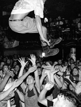 Czarno-białe zdjęcie zatłoczonego klubu, nad uczestników wyskakuje jeden z słuczaczy.