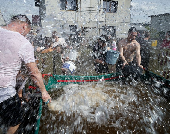 Wszędzie leje się woda, nawet na obiektyw. Kilku mężczyzn w koszulkach lub bez koszulek oblewa się wiadrami pełnymi wody.
