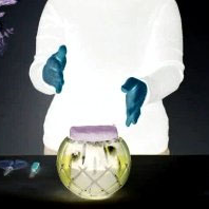 Negatyw. Na stole wazon w kształcie kuli, za nim postać, w tle bukiet kwiatów.