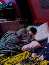 Najprawdopodobniej kobieta śpi pod kocem w jakim miejscu dla uchodźców.