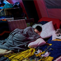 Najprawdopodobniej kobieta śpi pod kocem w jakim miejscu dla uchodźców.