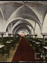 To jest zdjęcie dużego stołu do jadalni. Widać na nim oznaki starości. Na środku sali znajduje się czerwony dywan.