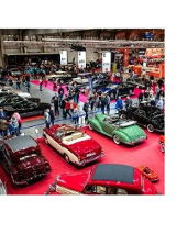 Zabytkowe samochody i zwiedzający na hali targowej.