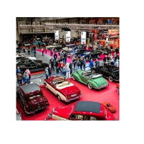 Zabytkowe samochody i zwiedzający na hali targowej.