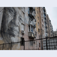 Kadr z filmu Piotra Armianovskiego, przedstawiający blok mieszkalny z muralem (ludzka twarz)