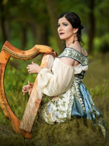 Na zdjęciu Barbara Karlik z harfą na łące, w pięknej sukni