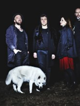 Zdjęcie przedstawia zespół muzyczny złożony z trzech mężczyzn i jednej kobiety oraz biały pies rasy husky na pierwszym planie.