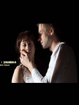 Aktorzy w trakcie spektaklu: mężczyzna dotyka lewą dłonią twarzy kobiety i patrzy na nią. Po lewej białe napisy z tytułem spektaklu