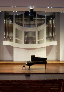 Zdjęcie przedstawia scenę auli Akademii Muzycznej w Poznaniu. Na środku sceny ustawiony jest fortepian. W tle widoczne piszczałki organów.