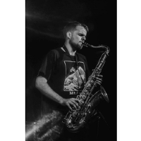 Czarno biała fotografia przedstawia profil młodego mężczyzny grającego na saksofonie.
