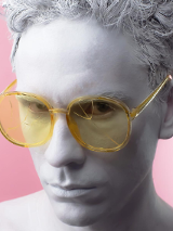 Zdjęcie przedstawia szarą twarz artysty w żółtych okularach.