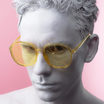 Zdjęcie przedstawia szarą twarz artysty w żółtych okularach.