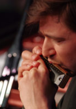 Zdjęcie twarzy mężczyzny grającego na harmonijce.