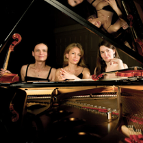 Na zdjęciu trzy kobiety siedzące przy fortepianie