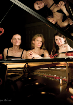 Na zdjęciu trzy kobiety siedzące przy fortepianie