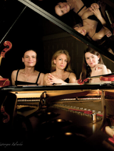 Na zdjęciu trzy kobiety siedzące przy fortepianie