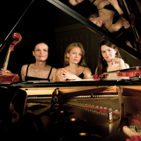 Na zdjęciu trzy kobiety siedzące przy fortepianie