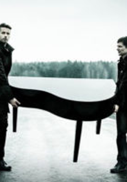 Na czarno-białym zdjęciu dwóch mężczyzn niosących fortepian.