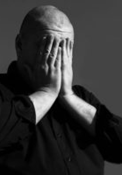 Na czarno-białym zdjęciu mężczyzna zakrywający twarz rękoma.